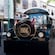 A vintage road train with the letters ‘H B E’ parked on a brick street surrounded by shops